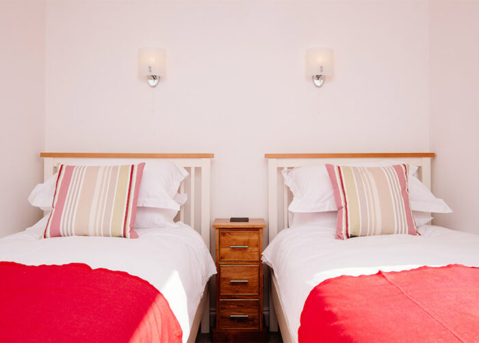 A twin bedroom at Highcliffe Holiday's Scarlett cottage, with red throws over the beds.